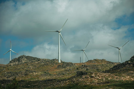 Wind turbines for electric power generation over green hilly landscape with rocks, in a sunny day...
