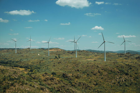 Several wind turbines for electric power generation over green hilly landscape with rocks, in a...