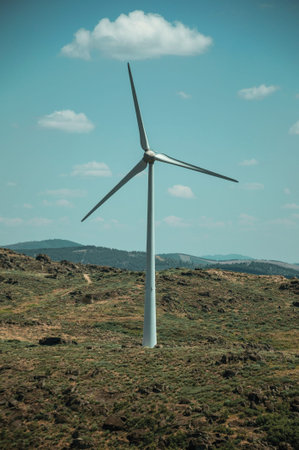 Single wind turbine for electric power generation over green hilly landscape with rocks, in a sunny...