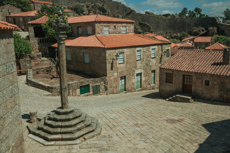 Stone gothic houses and chapel encircling a deserted square on slope with pillory, in a sunny day at...