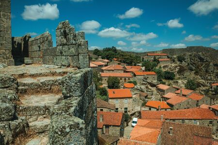 Pathway over thick stone wall next to rooftops of old houses and leafy trees, in a sunny day at the Sortelha Castle. One of the most astonishing and well preserved medieval villages in all Portugal.の写真素材