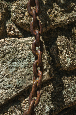 Close-up of iron chain stuck in a stone brick wall on a gothic house, in a sunny day at Sortelha....