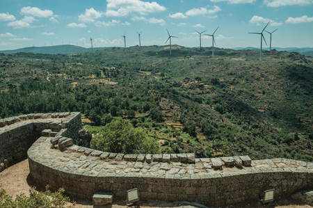 Pathway on thick stone wall with wind turbines over green hilly landscape, in a sunny day at the Sortelha Castle. One of the most astonishing and well preserved medieval villages in all Portugal.のeditorial素材