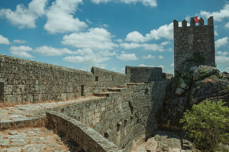 Pathway over thick stone wall with square tower from keep, in front of green rocky courtyard at the Sortelha Castle. One of the most astonishing and well preserved medieval villages in all Portugal.のeditorial素材
