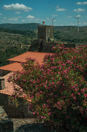 Flowered leafy trees and Castle over rocky cliff on hilly landscape with wind turbines, in a sunny day at Sortelha. One of the most astonishing and well preserved medieval villages in all Portugal.のeditorial素材