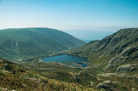 Blue fresh water at dam lake on hilly landscape covered by rocks and brushwood, on the highlands at the Serra da Estrela. The highest mountain range in continental Portugal, with astonishing scenery.の写真素材