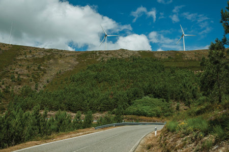 Countryside road passing through hilly landscape with several wind turbines, in a sunny day at Serra...