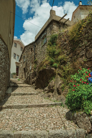 Old stone wall and houses in cobblestone alley on slope with steps, in a sunny day at Alvoco da...
