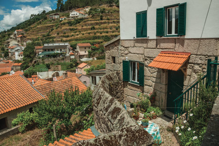 Facade of neat house and hilly landscape with trees and terraced fields, in a sunny day at Alvoco da...