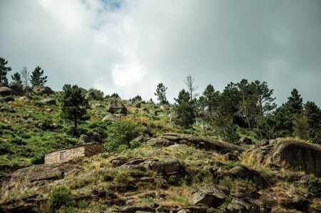 Rustic stone house on a hilly landscape with rocks and bushes, in a cloudy day near Loriga. Known as the Portuguese Switzerland for its landscape at Serra da Estrela highland on eastern Portugal.の写真素材