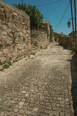 Old stone wall with dry bushes and old houses facades on narrow deserted alley, in a sunny day at Belmonte. A cute small town, birthplace of the navigator Pedro Alvares Cabral, on eastern Portugal.の写真素材