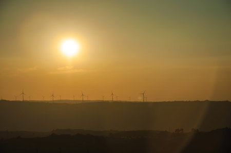 Hilly landscape and several wind turbines silhouettes for electric power generation, on sunset at Guarda. This friendly and well-kept medieval town is the highest in the continental Portugal.の写真素材