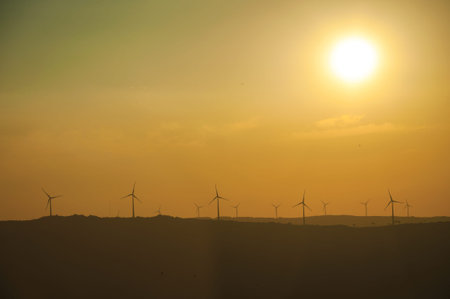 Hilly landscape and several wind turbines silhouettes for electric power generation, on sunset at...