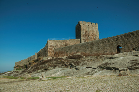 Stone wall with gateway and towers over rocky hill, in a sunny day at the Linhares da Beira Castle. A medieval hamlet with unique architectural diversity fruit of several times, in eastern Portugal.のeditorial素材