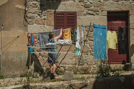 Belmonte, Portugal - July 16, 2018. Old woman hanging clothes to dry in front of old house at Belmonte. A cute small town, birthplace of the navigator Pedro Alvares Cabral, on eastern Portugal.のeditorial素材