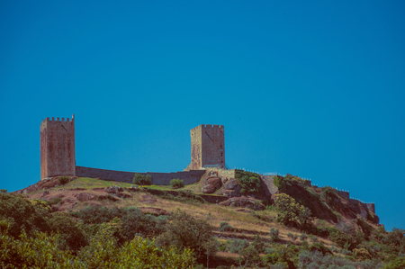 Hilly landscape with trees and rocks and the towers of Linhares da Beira Castle. A medieval hamlet with unique architectural diversity fruit of several times, in eastern Portugal. Vintage filter.のeditorial素材