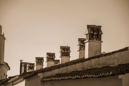 Several chimneys over rooftop of old house with worn plaster wall, at sunset in Marvao. An amazing medieval fortified village perched on a granite crag in eastern Portugal. Black and white photo.の写真素材