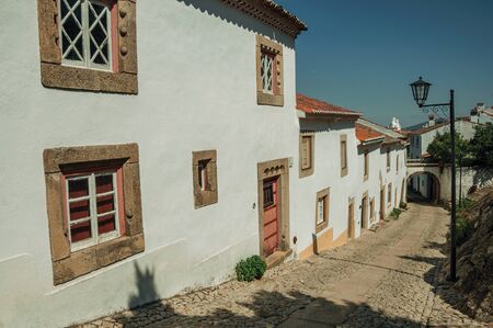 Charming facade of old houses with whitewashed wall in cobblestone alley on the way down, in a sunny day at Marvao. An amazing medieval fortified village perched on a granite crag in eastern Portugal.の写真素材