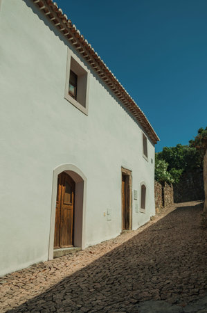 Charming facade of old house with whitewashed wall and wooden door in cobblestone alley, on sunny day at Marvao. An amazing medieval fortified village perched on a granite crag in eastern Portugal.の写真素材
