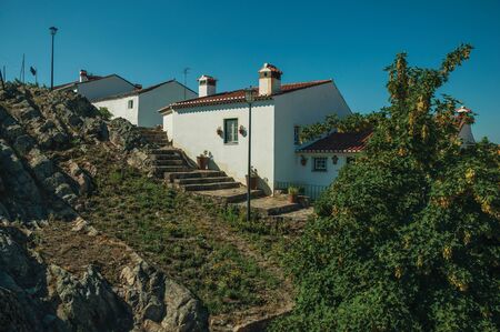 Old houses with whitewashed wall over rocky ridge, with stairs and leafy trees in a sunny day at Marvao. An amazing medieval fortified village perched on a granite crag in eastern Portugal.の写真素材