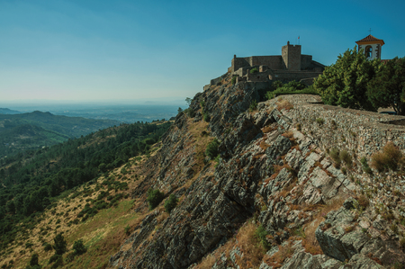 Stone wall and tower of Castle over ridge, with mountainous landscape covered by trees in a sunny day at Marvao. An amazing medieval fortified village perched on a granite crag in eastern Portugal.のeditorial素材