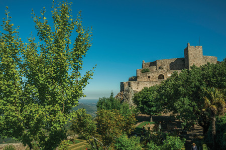 Stone walls and tower of Castle over rocky cliff in a sunny day, with lush wooden garden in the bottom at Marvao. An amazing medieval fortified village perched on a granite crag in eastern Portugal.のeditorial素材