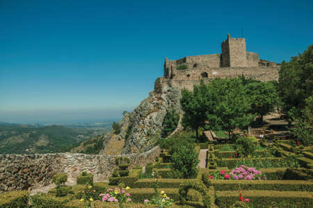 Stone walls and square tower of Castle over hill on sunny day, with flowered garden at Marvao. An amazing medieval fortified village perched on a granite crag in eastern Portugal. Retouched photo.のeditorial素材