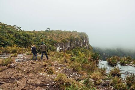 People on edge of cliff and mist coming up from the green valley at Serra Geral National Park near Cambara do Sul. A small rural town in southern Brazil with amazing natural tourist attractions.の写真素材