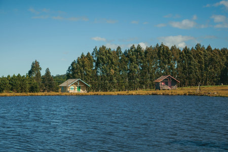 Charming wooden chalets facing a blue water lake in a hilly landscape with trees and dry bushes near Cambara do Sul. A small rural town in southern Brazil with amazing natural tourist attractions.の写真素材