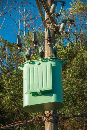 Detail of high-voltage power pole transformer with electrical wiring in front of trees near Gramado....