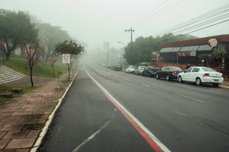 Bento Goncalves, Brazil - July 14, 2019. Quiet paved street with houses and parked cars, on a foggy...