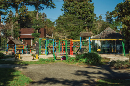 Gramado, Brazil - July 21, 2019. Colorful playground equipment among trees with children and adults...