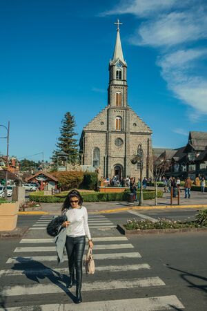 Gramado, Brazil - July 21, 2019. Woman crossing the Borges de Medeiros Avenue at the crosswalk in front of church in Gramado. A cute european-influenced town highly sought after by tourists.のeditorial素材