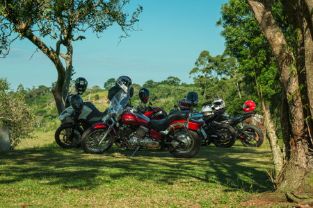Pardinho, Brazil - June 20, 2019. Several parked motorcycles under trees shade, on hilltop covered...