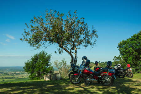 Pardinho, Brazil - June 20, 2019. Several parked motorcycles under trees shade, on hilltop covered by meadow in a sunny day near Pardinho. A small rural village in the countryside of Sao Paulo State.のeditorial素材