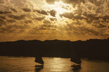 Cloudy sky with sunshine and traditional sailing boats called felucca sailing the Nile river. The largest watercourse on earth that crosses Egypt from south to north.の写真素材