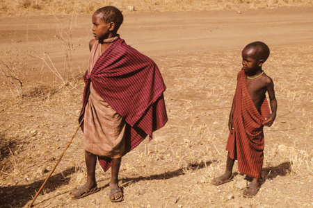 Serengeti, Tanzania - February 10, 1997. Inquisitive Maasai children dressed in typical clothes at Serengeti. A huge national park in the African savanna where several species of large mammals live.のeditorial素材