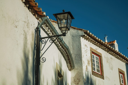 Wrought iron streetlight stuck to a plaster wall from an old house at sunset in Marvao. An amazing...