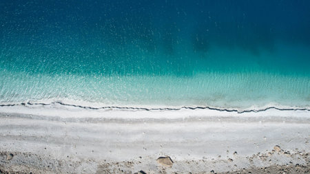 Aerial top-down view of the stunning turquoise and deep blue waters of Lake Salda, Turkey, from directly above the white mineral beach. This direct overhead perspective highlights