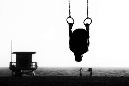Silhouette of a person swinging on rings on the beach, Santa Monica Beach, Santa Monica, Los Angeles County, California, USAの写真素材