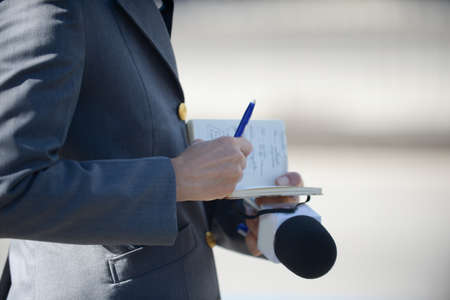 reporter writing his notes in a notebook and holding the microphoneのeditorial素材
