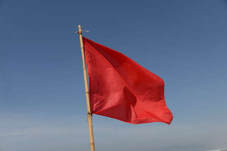 red flag swaying in the wind on a blue sky background.のeditorial素材