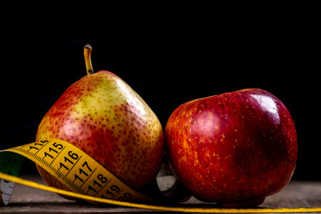 healthy diet; pear and apple with measure tape over black background