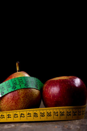 healthy diet; pear and apple with measure tape over black backgroundの写真素材