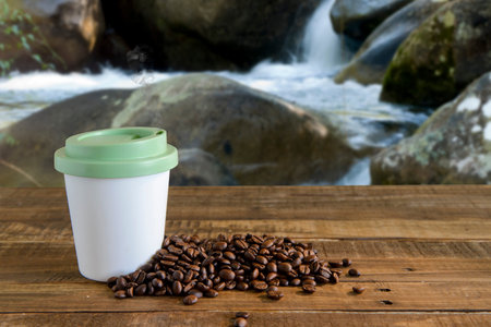coffee mug with beans beside on table near waterfall
