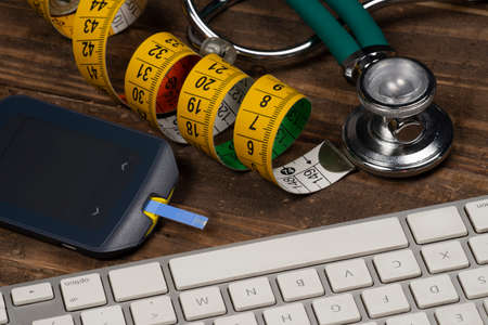 glucose meter, keyboard, tape measure and stethoscope on wooden tableの写真素材