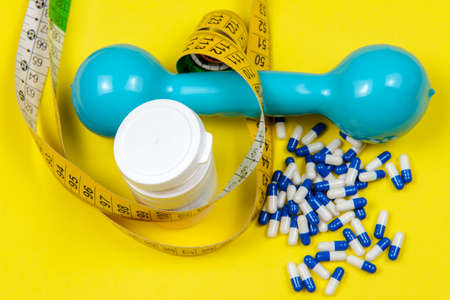 Yellow measuring tape around a white bottle of pills, tablets on yellow background, slimming and testosterone concept. Top viewの写真素材