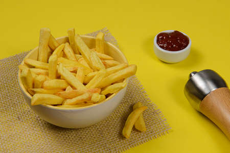 portion of potato fries in ceramic bowl on yellow backgroundの写真素材