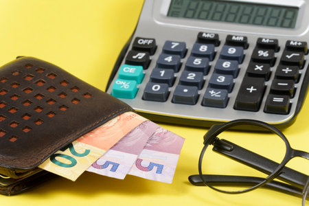 money coming out of wallet with blurred pocket calculator in the background.