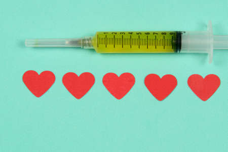 syringe next to red heart paper designs in a light green backgroundの写真素材